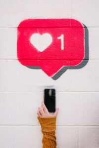 Social media heart symbol painted above someone's arm holding a cell phone